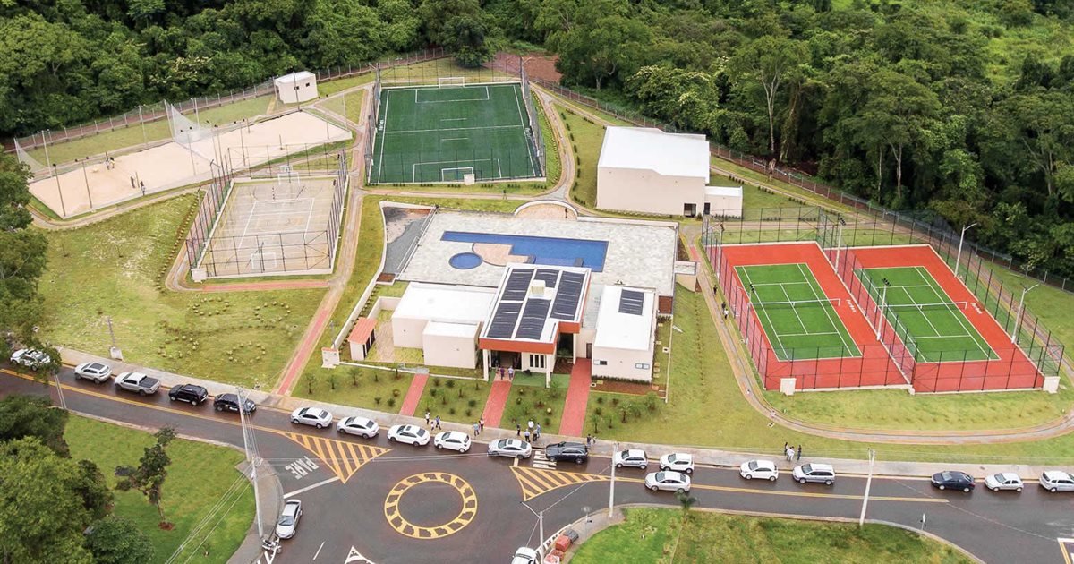 Vista aérea da área de lazer de um condomínio em Anápolis, com campo de futebol, quadras, piscina, clube e quadras de tênis cercados por mata.